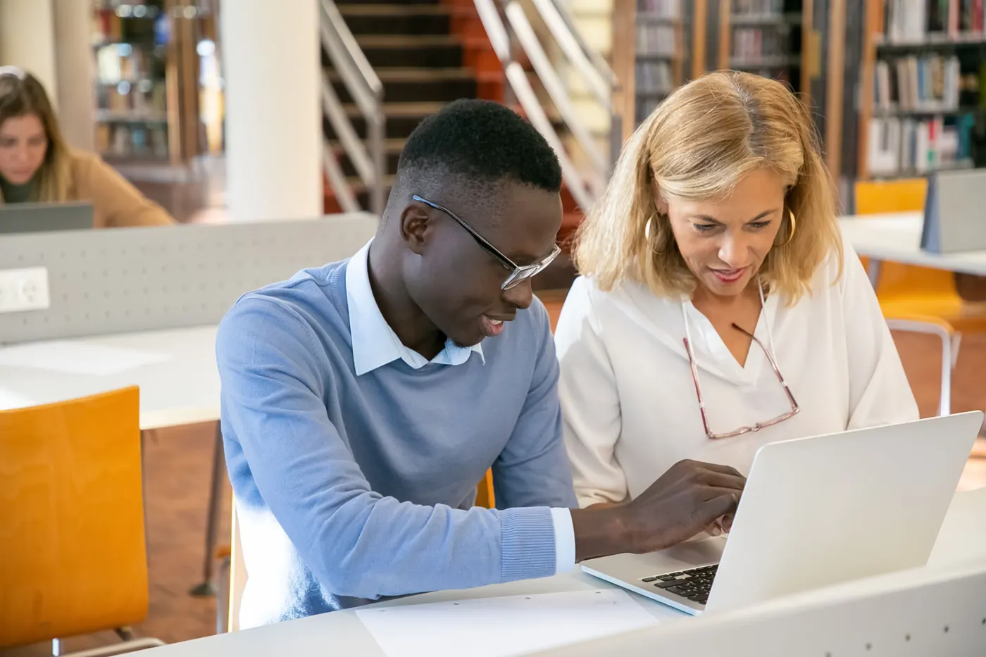 A mentor and a student looking at work together on a laptop in a school library