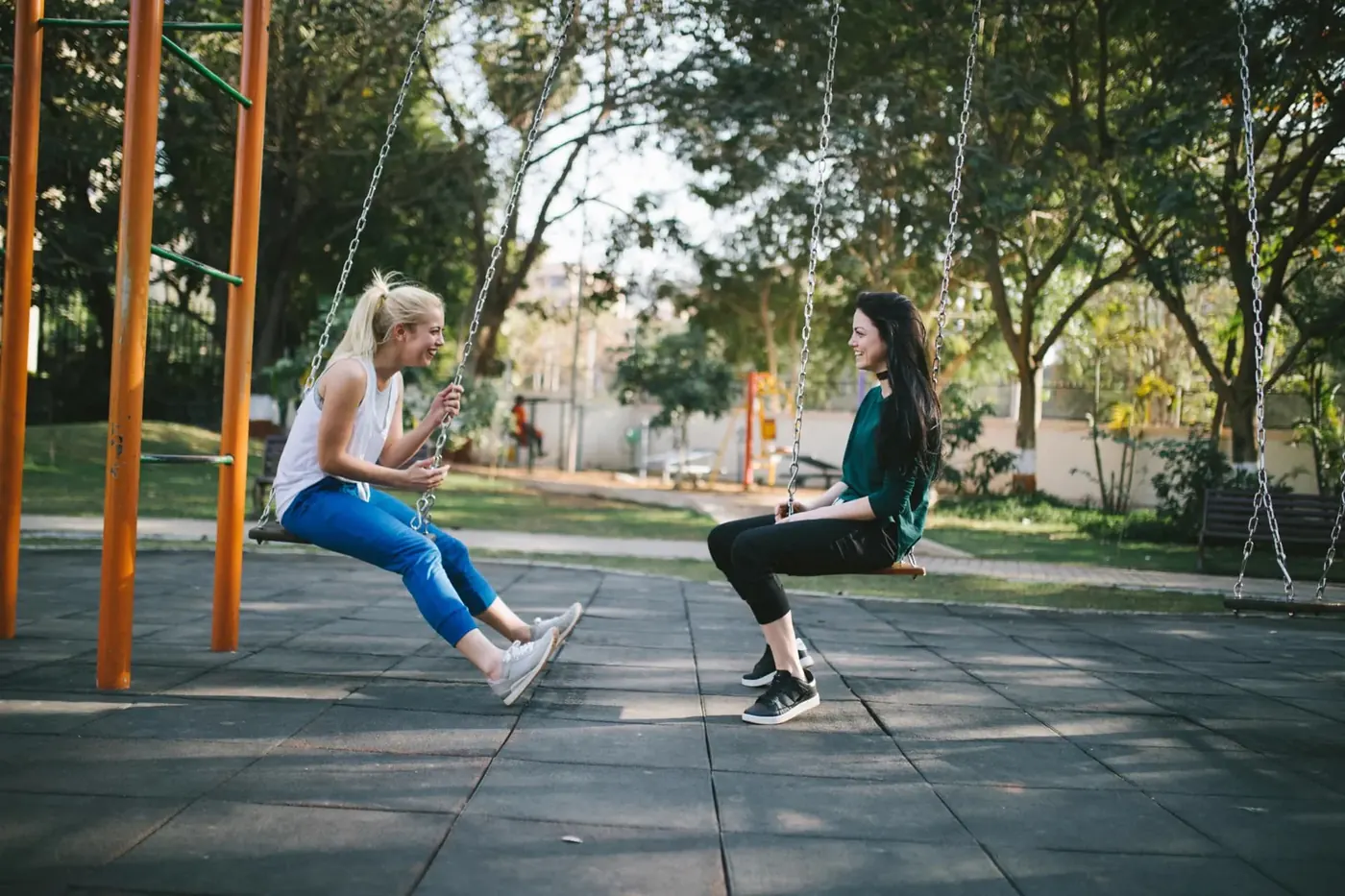 Two people talking on swings outdoors in afternoon sunlight