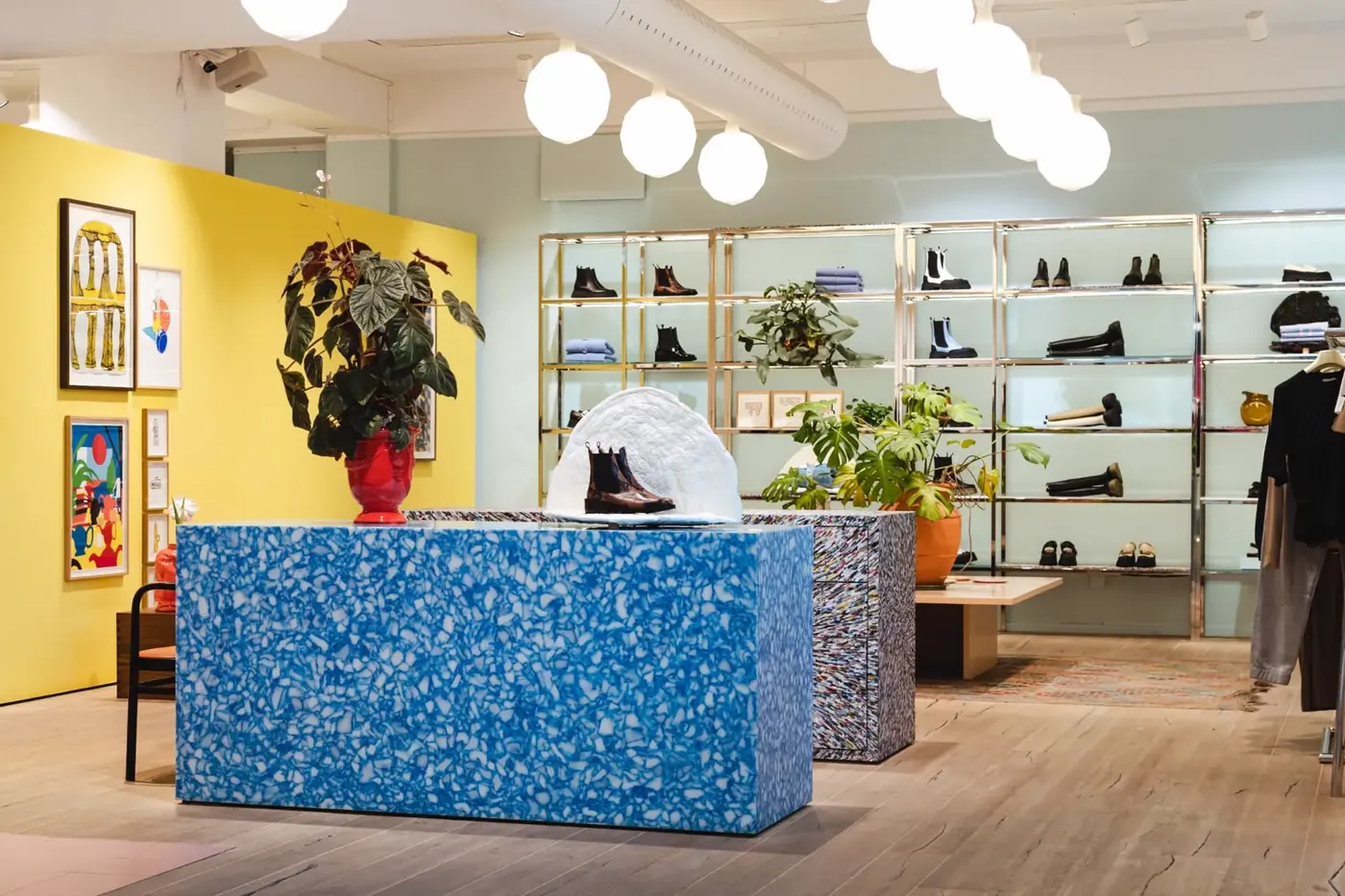 A bright Stockholm concept store with a blue terrazzo counter, yellow wall and glass shelving