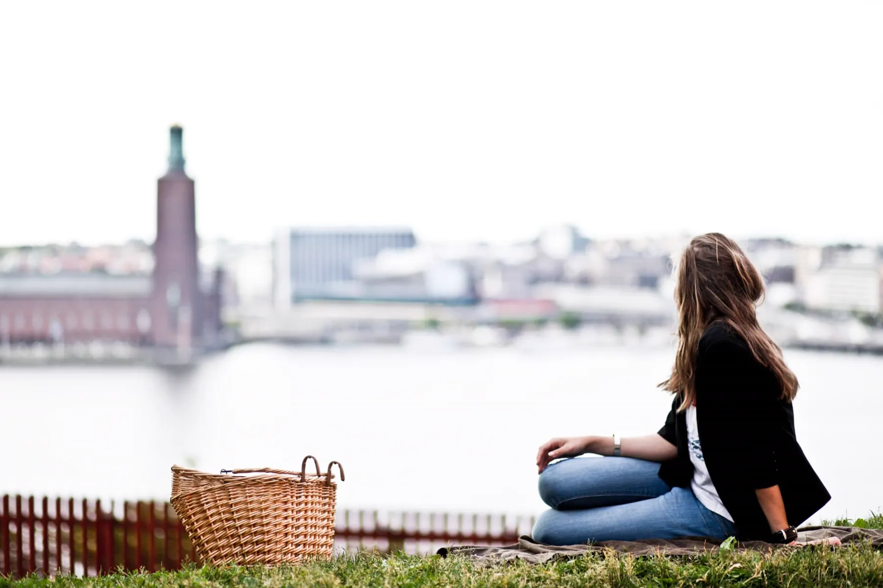 A woman sitting on the grass above the water looking across to Stockholm City Hall
