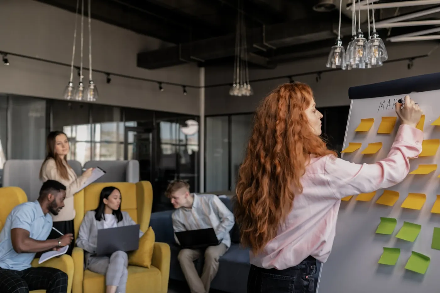 A woman writing on a flipchart with sticky notes while colleagues work nearby