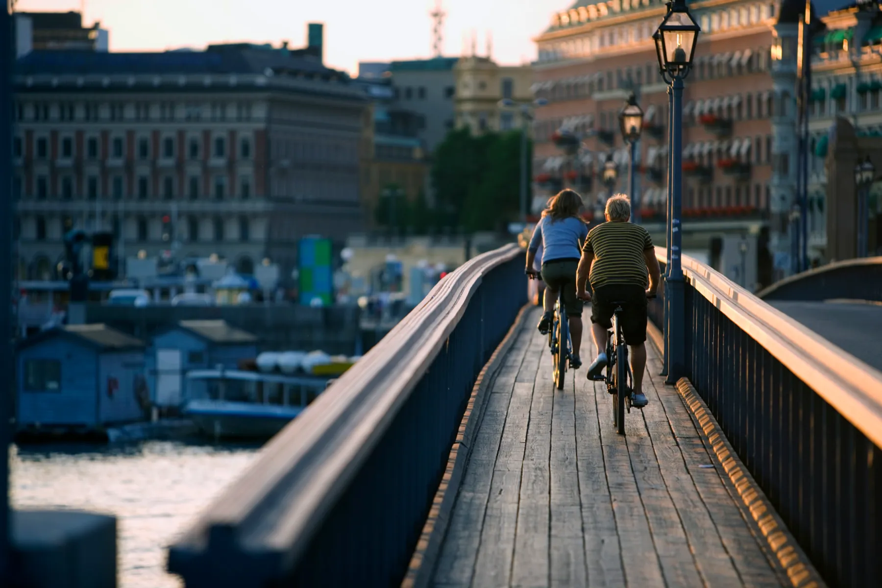 Two cyclists riding across a wooden bridge in central Stockholm at golden hour