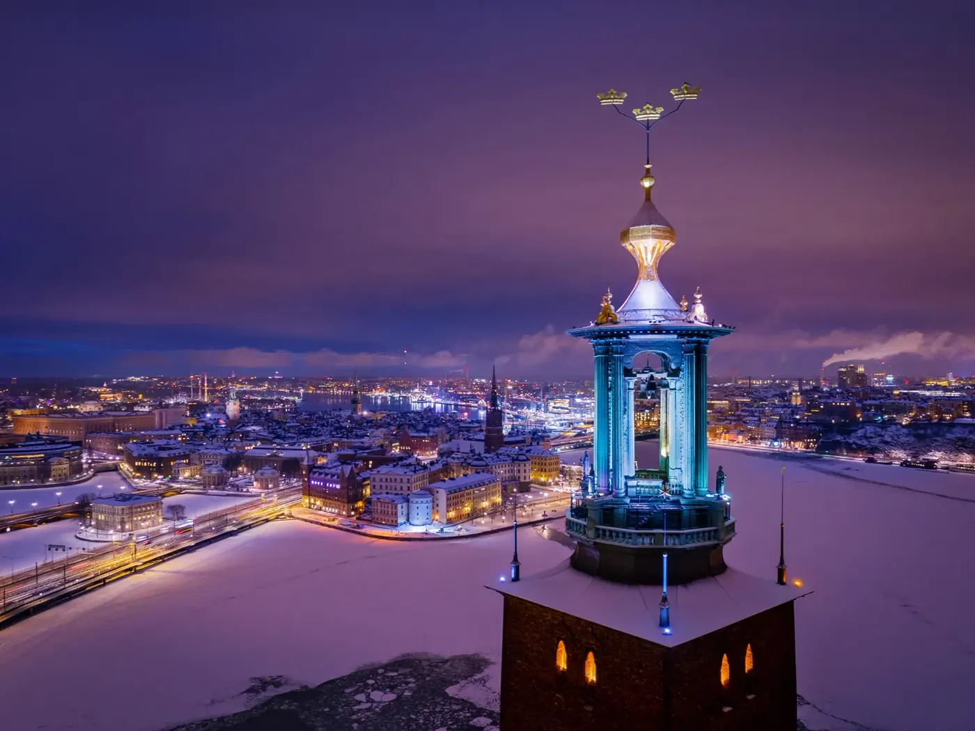 Stockholm City Hall tower lit above a snow-covered city at dusk